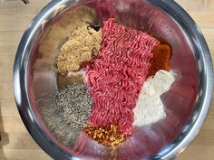 a metal bowl filled with different types of meat and seasonings on top of a wooden table