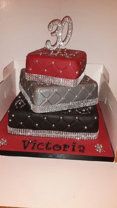 a red and black cake sitting on top of a white box filled with silver decorations