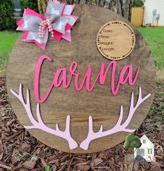 a wooden sign that says carina with pink and white antlers on it, in front of a tree