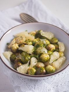 a white bowl filled with brussel sprouts and other vegetables next to a fork