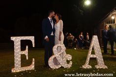 a bride and groom kissing in front of letters that spell out e & a at night