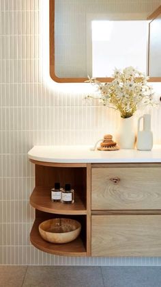 a bathroom with a wooden cabinet, mirror and vase on the sink counter next to it