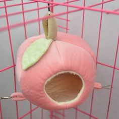 a pink bird cage with a stuffed apple hanging from it's side and a green leaf on top