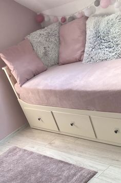 a bed that has some pillows on top of it in a room with pink walls