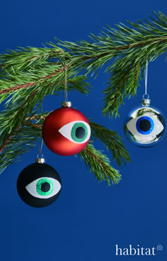 two ornaments hanging from a pine tree with an evil eye ornament on it