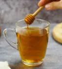 a person holding a honey stick over a cup of tea