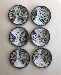 four black and white plates sitting on top of a table next to each other with holes in them