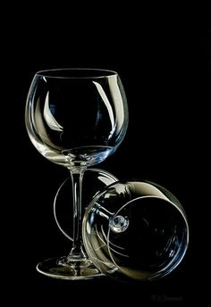 two wine glasses sitting next to each other on a black background with one glass half empty