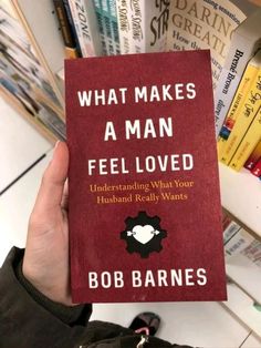 a person holding up a book in front of bookshelves with the title what makes a man feel loved