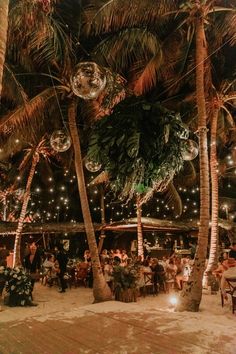 people sitting at tables under palm trees with lights on them and disco balls hanging from the ceiling