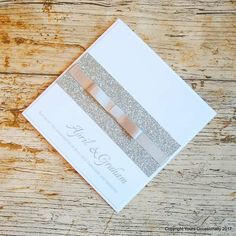 a wedding card with glitter and ribbon on top of a wooden table in front of a piece of wood