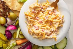 a white plate topped with pasta salad next to sliced cucumbers and crackers