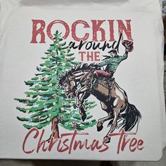 a t - shirt that says rockin around the christmas tree with a cowboy riding a horse