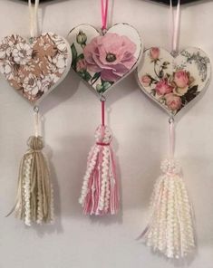 four heart shaped ornaments hanging on a wall with tassels attached to the strings