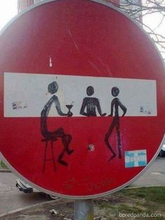 a red and white street sign with people sitting at a table painted on the side