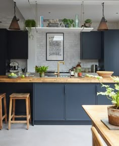 a kitchen with blue cabinets and wooden stools next to a counter top that has potted plants on it