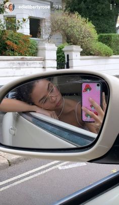 a woman taking a selfie in the side mirror of a car with her cell phone