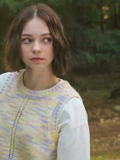 a woman standing in the woods wearing a yellow and blue knitted sweater with short sleeves