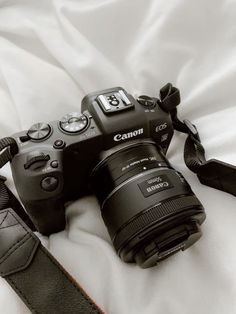 a canon camera sitting on top of a bed next to a black leather case and strap