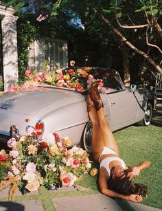 a woman laying on the ground next to a car with flowers growing out of it