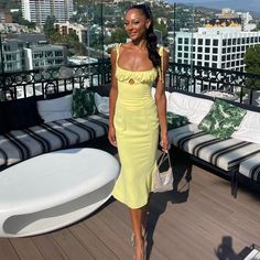 a woman in a yellow dress is standing on a balcony with couches and tables