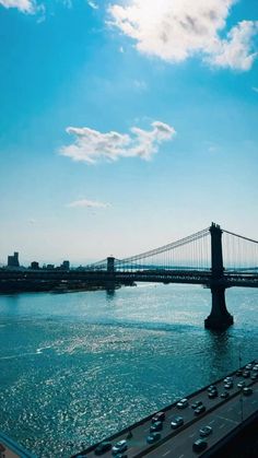 cars are driving on the road by the water and bridge in the distance with blue sky above