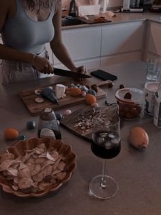 a woman cutting up food on top of a wooden table next to a glass of wine