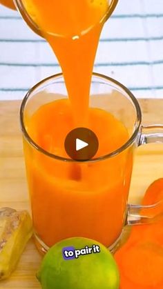 orange juice being poured into a glass with fruit around it on a wooden table top