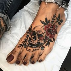 a woman's foot with a skull and flower tattoo on it, sitting on a bed