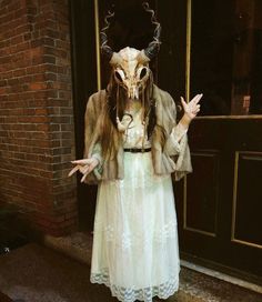 a woman dressed up as a demon standing in front of a door with her hands out