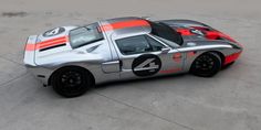 a silver and orange sports car parked on top of a cement parking lot next to an airport