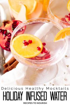 Photo of a champagne glass filled with water and pomegranate arils and a orange slice floating in it and an orange slice on the rim with another champagne glass and a glass pitcher sitting behind them filled with the infused water, silver garland around the glasses, a half a pomegranate and cinnamon sticks on a white towel and a silver spoon next to it with text that says Delicious Healthy Mocktails, Holiday Infused Water.