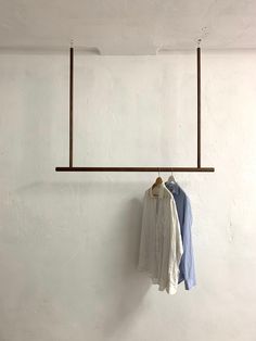 two shirts hanging on a clothes rack in front of a white wall with an iron bar