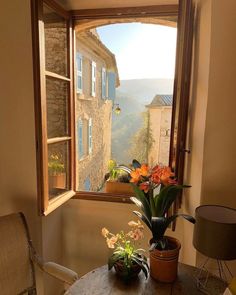 an open window with flowers on the table in front of it and a view of mountains outside