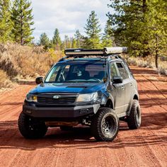 a truck is parked on the side of a dirt road with trees in the background