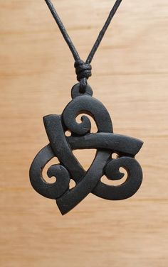 a black pendant with an intricate design on a wooden surface, hanging from a cord