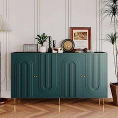 a green cabinet with gold legs and a clock on it's sideboard next to a potted plant