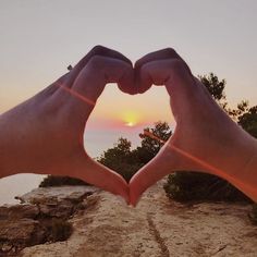 two hands making a heart shape with the sun setting in the background