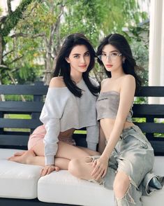 two young women sitting on top of a white couch next to each other in front of trees