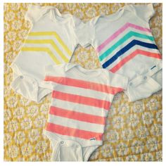 three baby onesuits with different colored stripes on them sitting on a yellow blanket