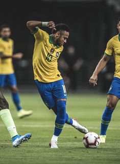 two soccer players in yellow and blue uniforms are kicking the ball while another player looks on