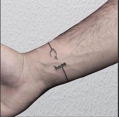 a small wrist tattoo with the word hope on it and a hand holding a cross