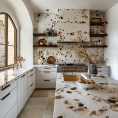 a kitchen with white cabinets and marble counter tops in front of an arched window that has brown spots on the wall