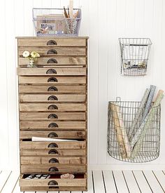 a wooden drawer with many drawers and baskets on the top, in front of a white wall