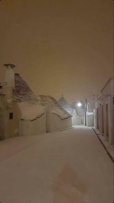 a snow covered street with buildings on both sides and a light at the end in the distance