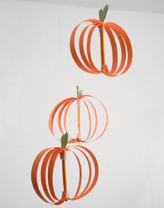 three orange paper pumpkins hanging from strings on a white wall in front of a window