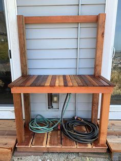 a wooden shelf sitting on the side of a house next to a hose and power cord