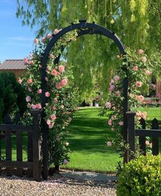 a black gate with pink roses growing on it in front of a green lawn and trees