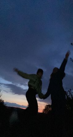 two people standing in the dark with their arms outstretched