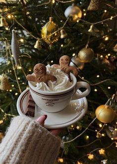 someone is holding a cup of coffee with cookies in it and the christmas tree behind them